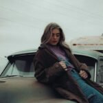 woman in brown coat sitting on car
